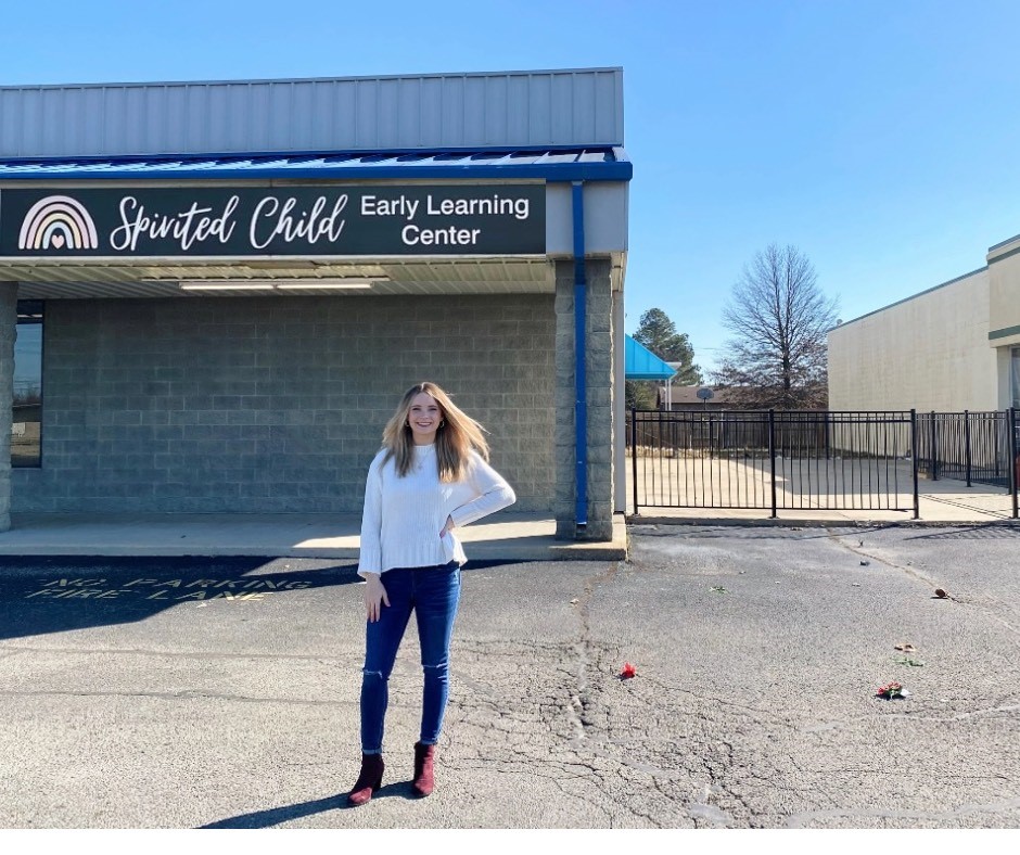 Krista Beard in front of her school and a sign that says Spirited Child Early Learning Center