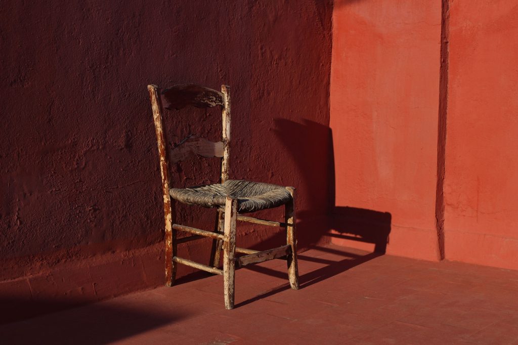 Old wooden one vintage chair in a room with red grunge walls and floor in sunlight, dark shadows.